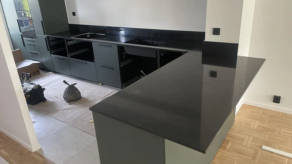 Køkkenbordplade og køkkenø i sort Silestone Night Tebas, poleret komposit, med uppvikt stænkplade i ett køkken under montering i Oxie.