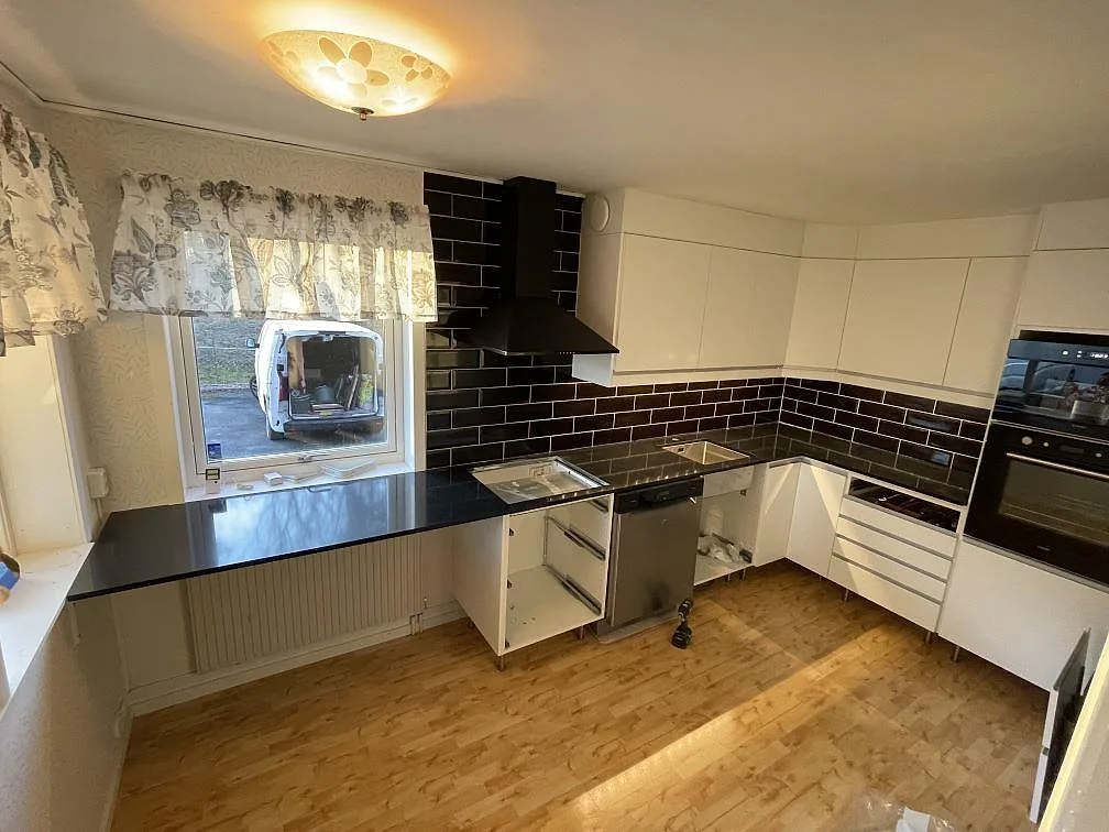 Køkkenbordplade i mørk Silestone Night Tebas, poleret kvartskomposit, i ett U-format køkken med vita skabe og mörkt kakel i Väddö.