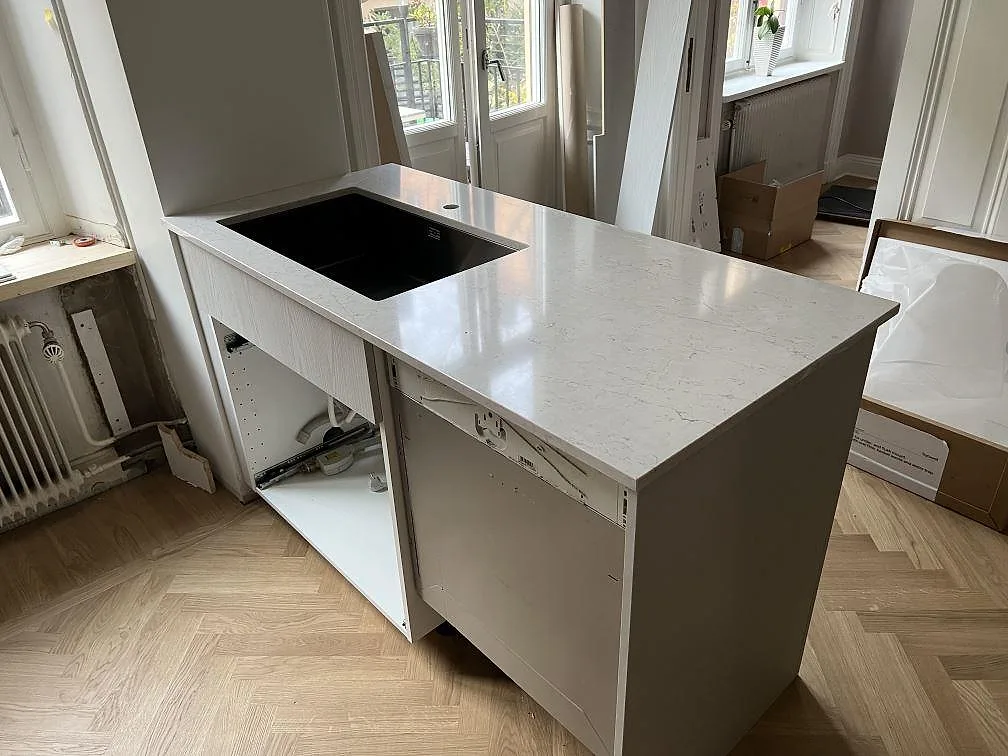 Køkkenbordplade i lys Silestone Pearl Jasmine, poleret kvartskomposit, på en bred bänkdel med mørk rektangulär urtagning under montering i Stockholm.