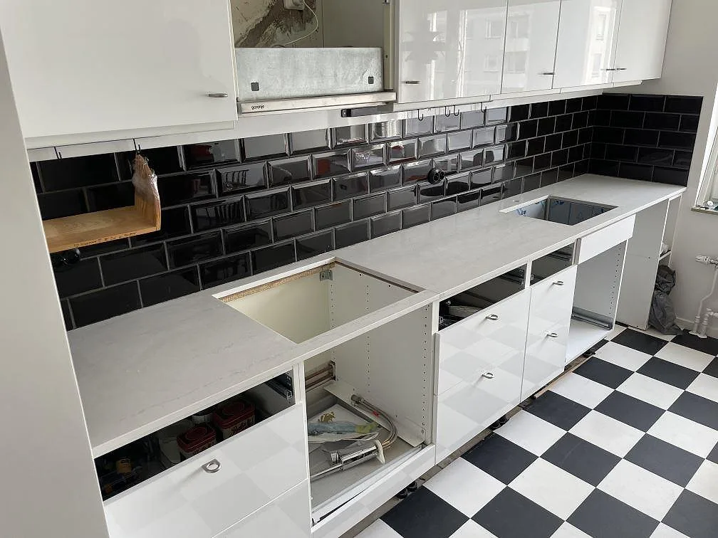 Køkkenbordplade i hvid Silestone Raw A, mat kvartskomposit, med hällöppning og sort kakelvägg i ett køkken i Lidingö.