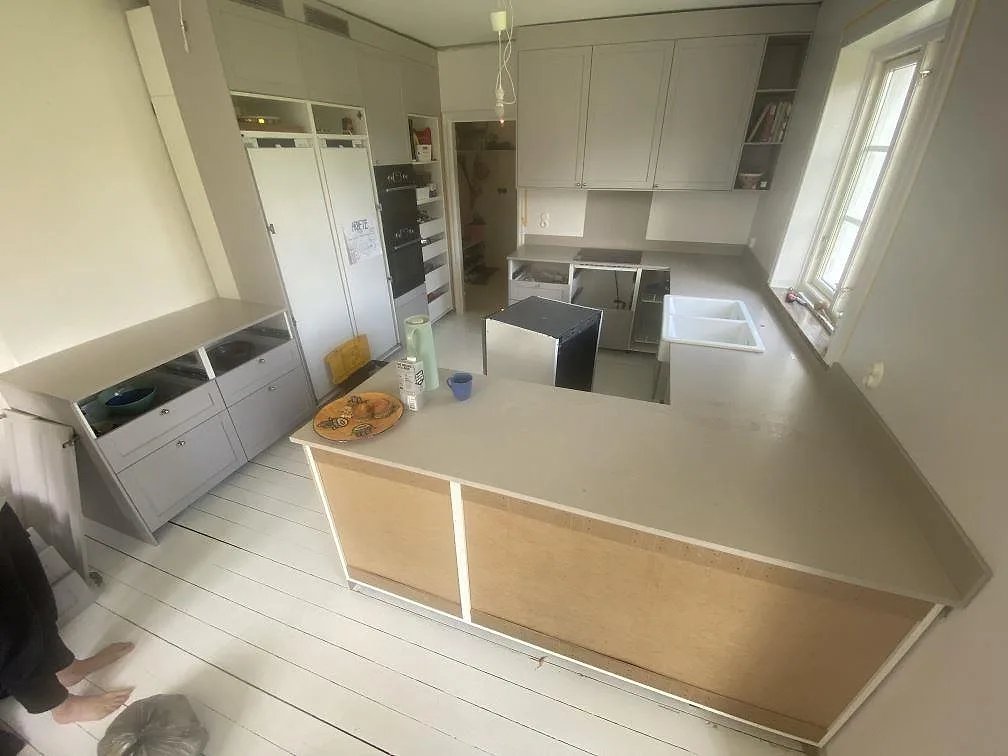 U-format køkken i Helsingborg med køkkenbordplader og en bred halvö i Silestone Royal Reef, en mat gråbeige kvartskomposit, med hvid keramikho og sort induktionshäll under montering.