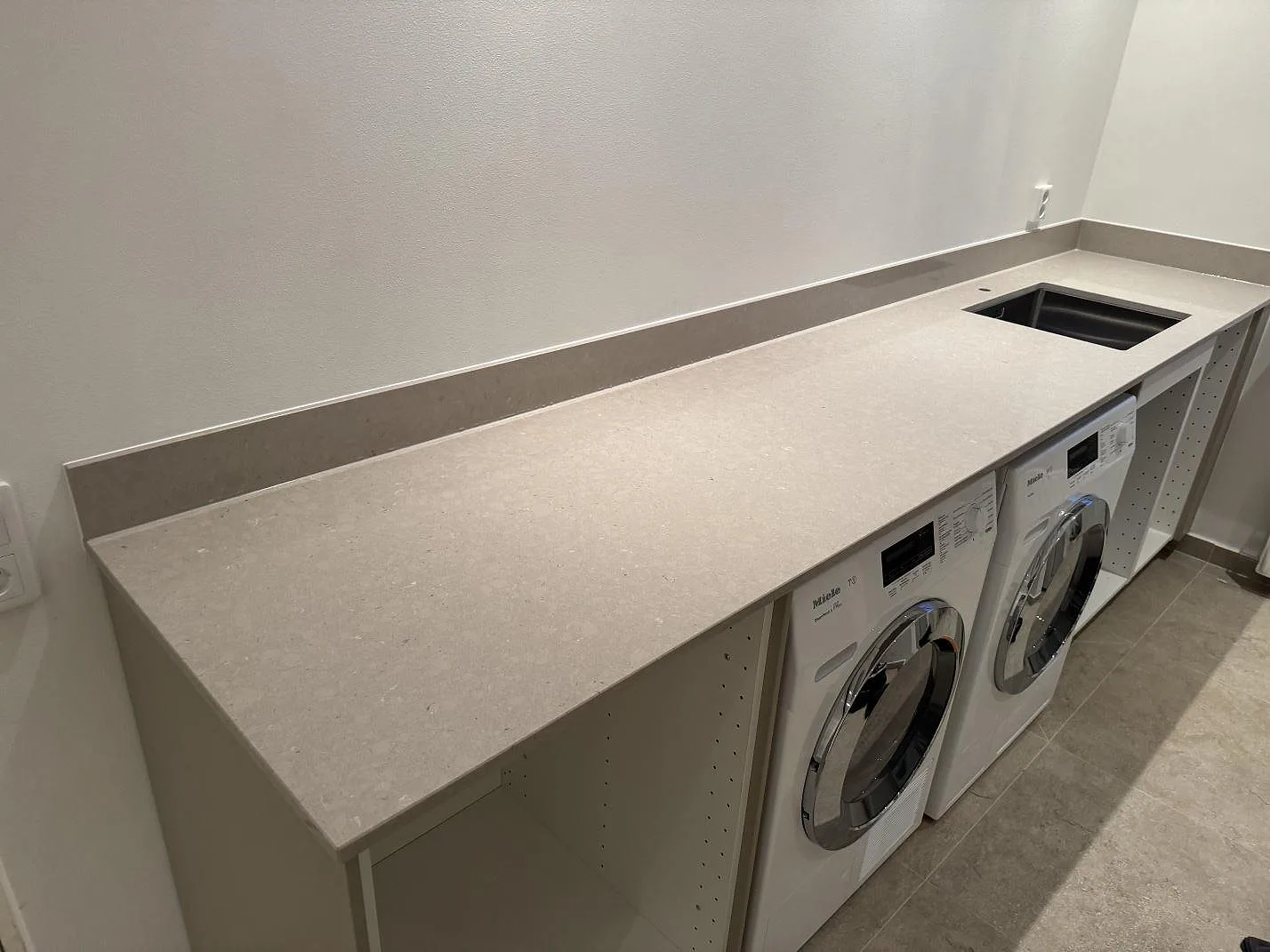 Bordplade i poleret Silestone Royal Reef med 12 mm stänkkant, rostfri vask og maskiner i ett tvättutrymme i Höllviken.