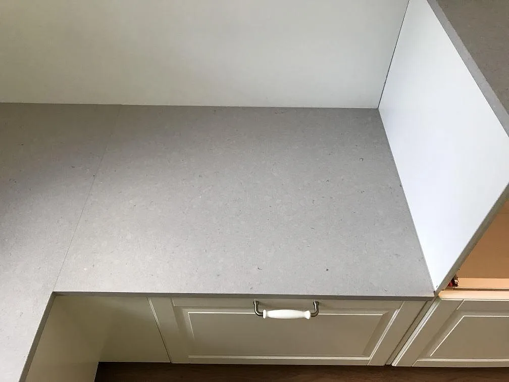 Køkkenbordplade i ljust gråmelerad Silestone Royal Reef, mat Mocka-finish, monteret på krämfärgade köksstommar i ett køkken i Olofström.