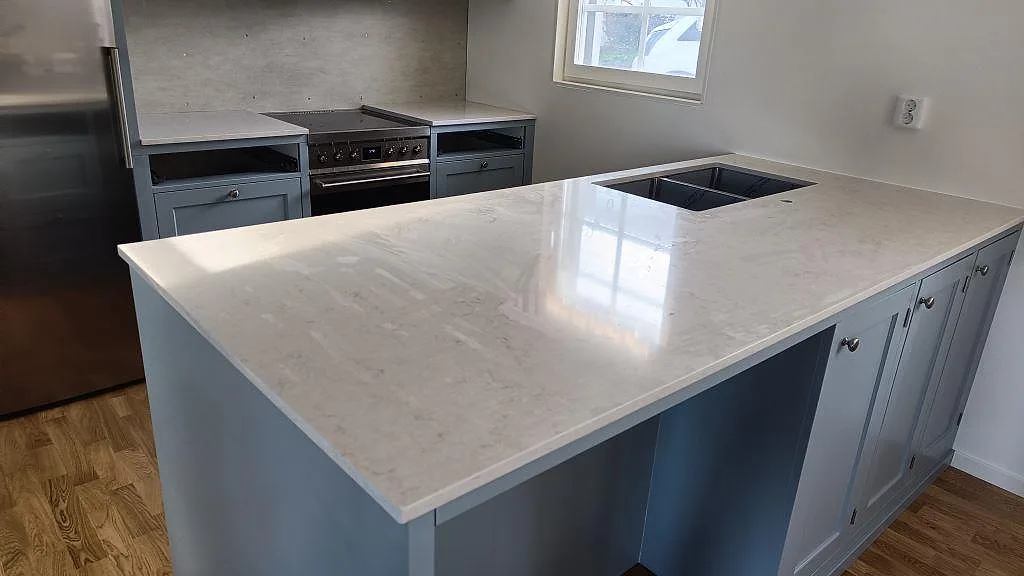 Køkkenø og bänkrad i poleret Silestone Snowy Ibiza, hvid kvartskomposit med rostfri vask og fristående komfur i ett køkken i Båstad.