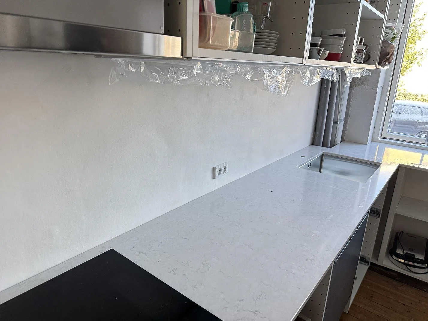 Køkkenbordplade i poleret Silestone Snowy Ibiza, hvid kvartskomposit, med sort kogeplade og rostfri vask i ett køkken i Bagsværd.