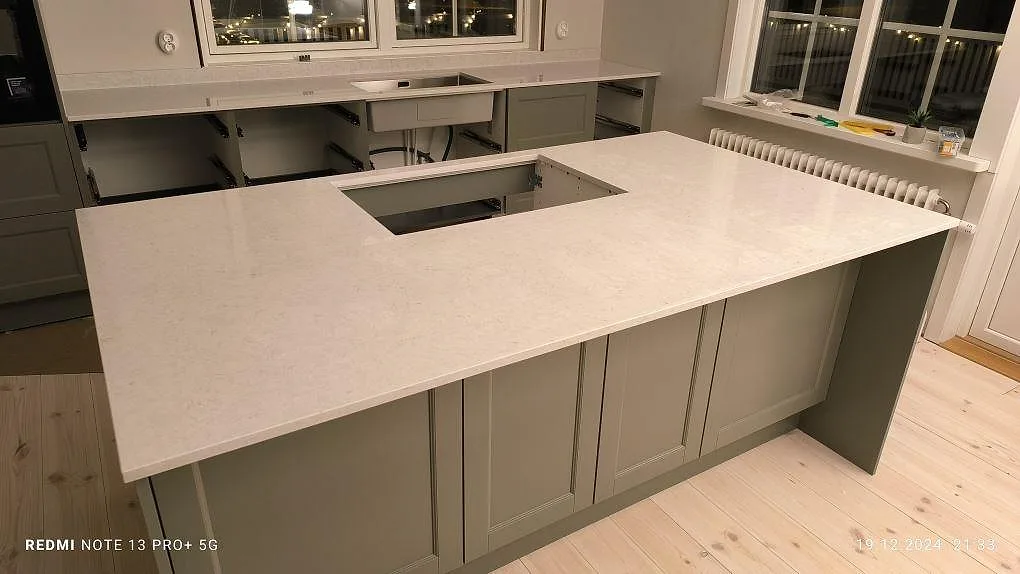 Køkkenbordplade i poleret Silestone Snowy Ibiza, lys kvartskomposit, med køkkenø og fönstersida i ett køkken i Bjursås under montering.