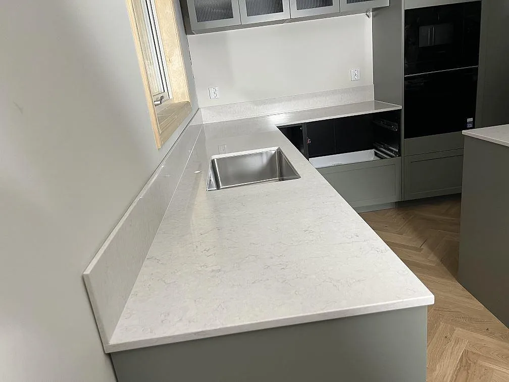 Køkkenbordplade i poleret Silestone Snowy Ibiza, kvartskomposit, med uppvikt stänkkant vid vindue i ett køkken i Enköping.