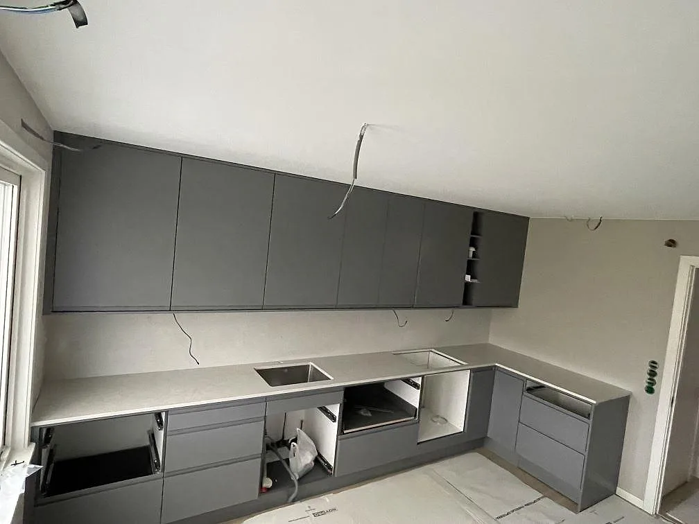 Køkkenbordplade i lys Silestone Snowy Ibiza, poleret, monteret i ett L-format køkken med mörkgrå skabe i Hässelby.
