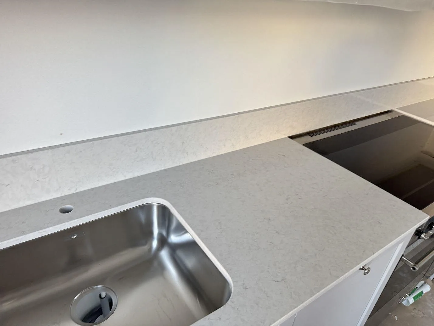 Køkkenbordplade i poleret Silestone Snowy Ibiza med rostfri vask, komfur og låg stänkkant i ett køkken i Karlshamn.