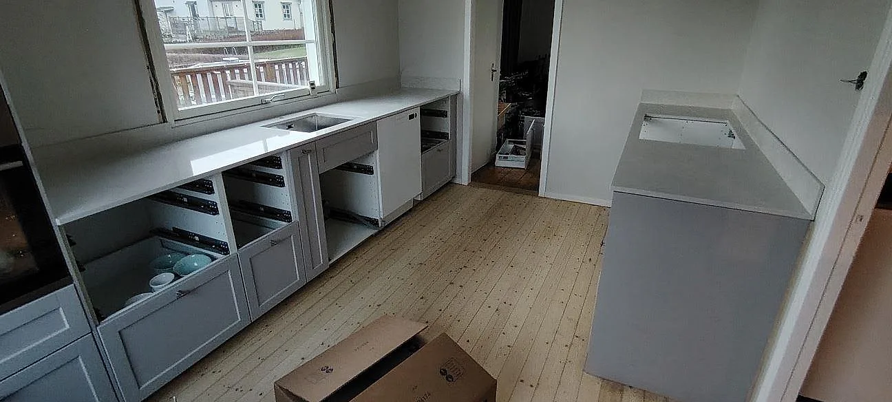 Poleret køkkenbordplade i hvid Silestone Snowy Ibiza vid vindue og separat bänkrad med låg stänkkant i ett køkken under montering i Kolbäck.