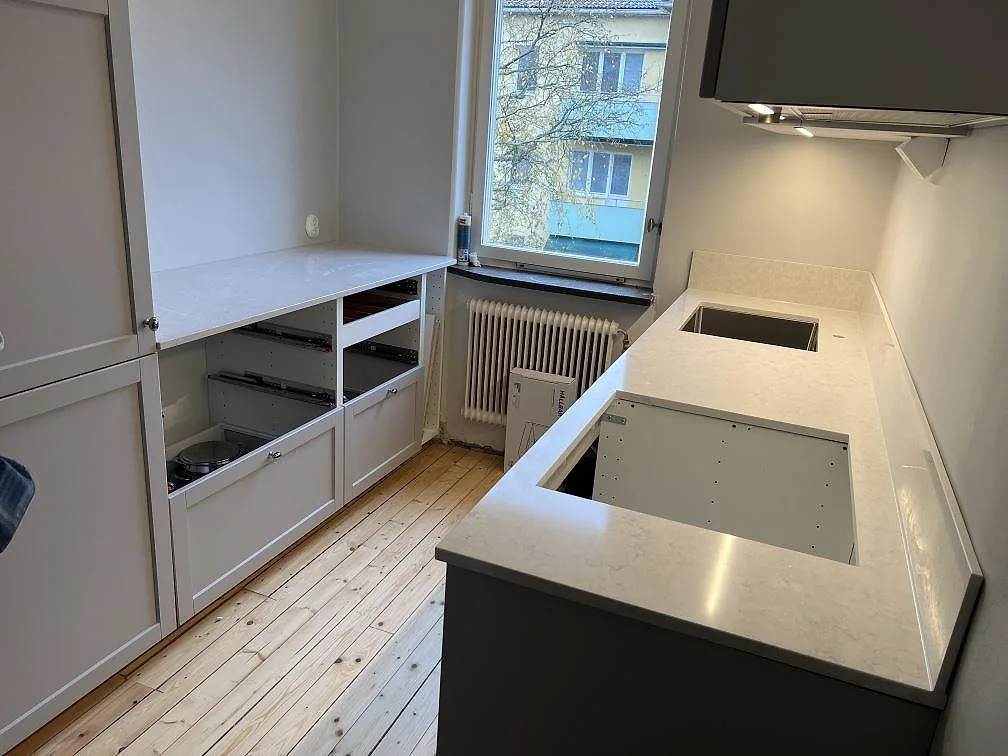 Poleret køkkenbordplade i hvid Silestone Snowy Ibiza, komposit, med hällurtag, stænkplade og sidobänk i ett køkken i Lidingö.
