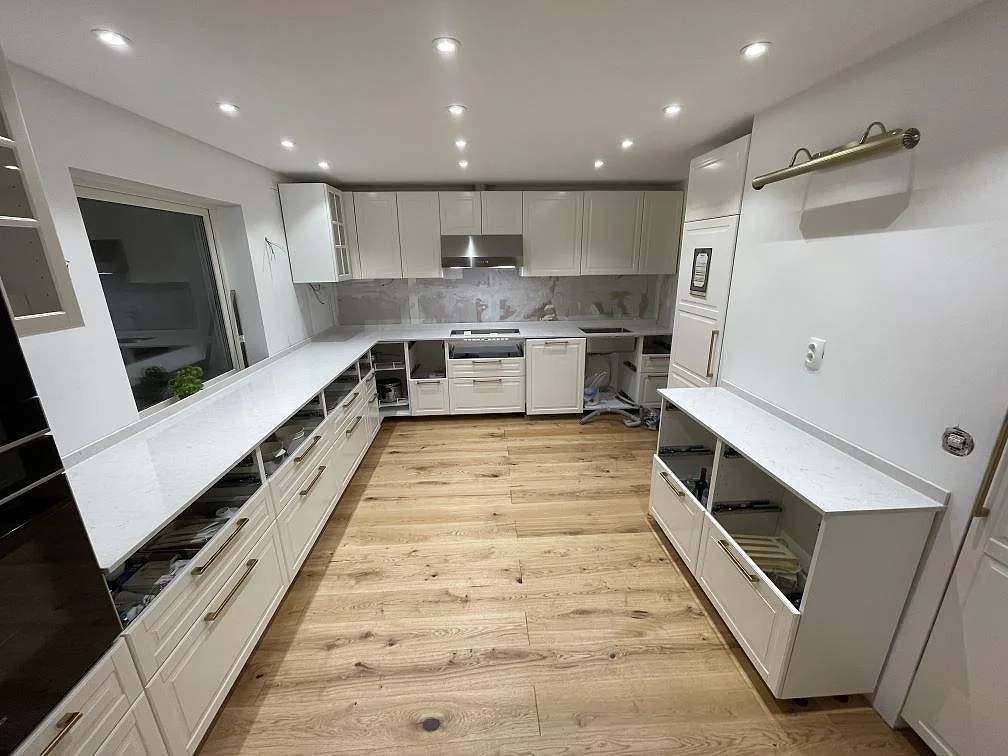 Køkkenbordplade i hvid Silestone Snowy Ibiza, poleret kvartskomposit, monteret rundt om ett U-format køkken med vita fronter og öppna skabe i Linköping.