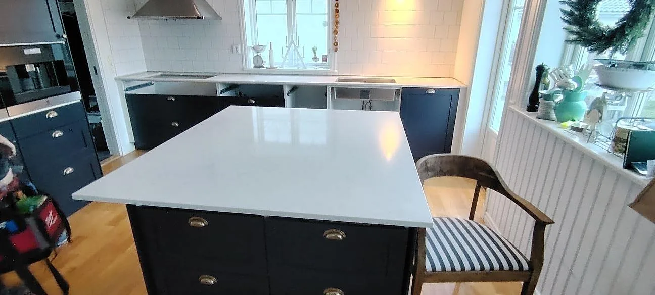 Poleret køkkenbordplade i lys Silestone Snowy Ibiza kvartskomposit som køkkenø og väggbänk i ett køkken med svarta fronter i Motala.