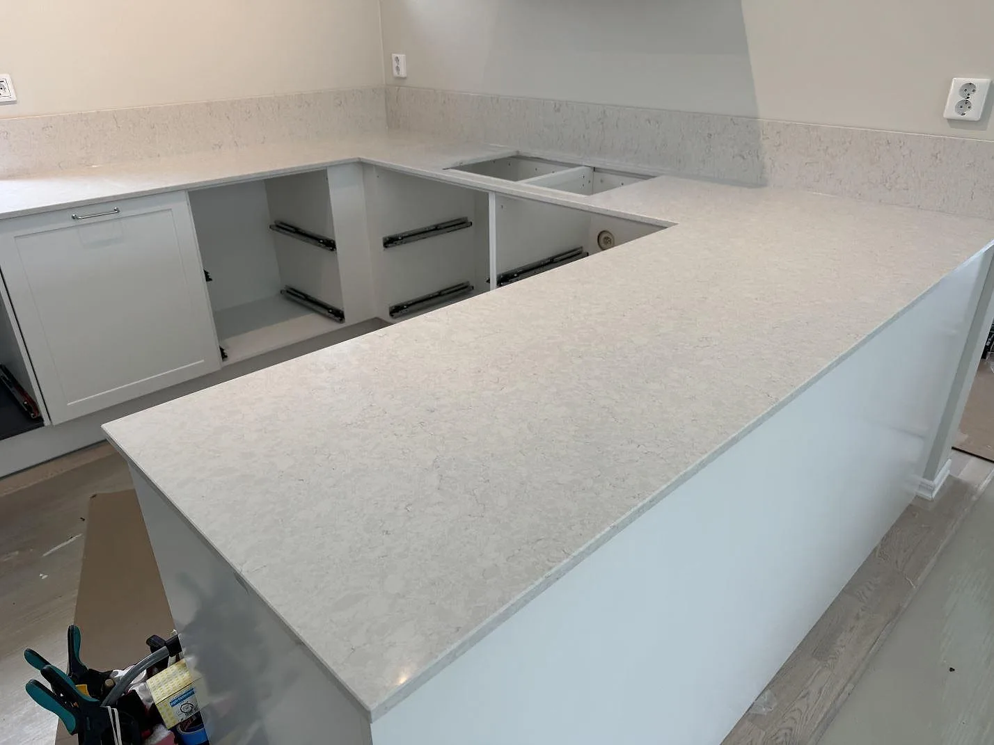 Køkkenbordplade i poleret Silestone Snowy Ibiza, lys kvartskomposit, med halvö og låg stänkkant i ett køkken i Nättraby under montering.