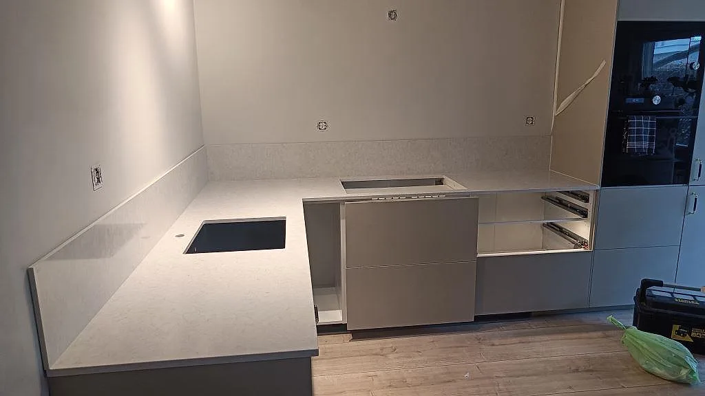 L-formad køkkenbordplade i poleret Silestone Snowy Ibiza med låg stänkkant, diskhozon og hällöppning i Rydebäck.