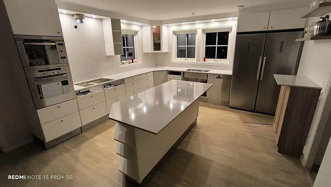 Køkkenbordplade og stor køkkenø i hvid poleret Silestone Snowy Ibiza komposit i ett ljust køkken under montering i Saltsjö Boo.