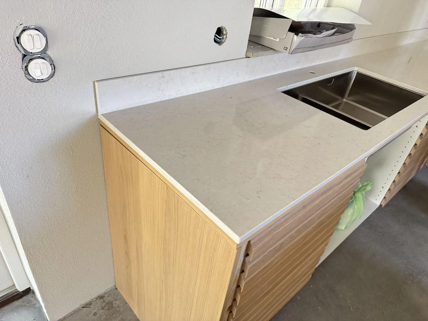 Køkkenbordplade i poleret Silestone Snowy Ibiza, hvid kvartskomposit, med låg stänkkant og rostfri vask i ett køkken under montering i Simrishamn.