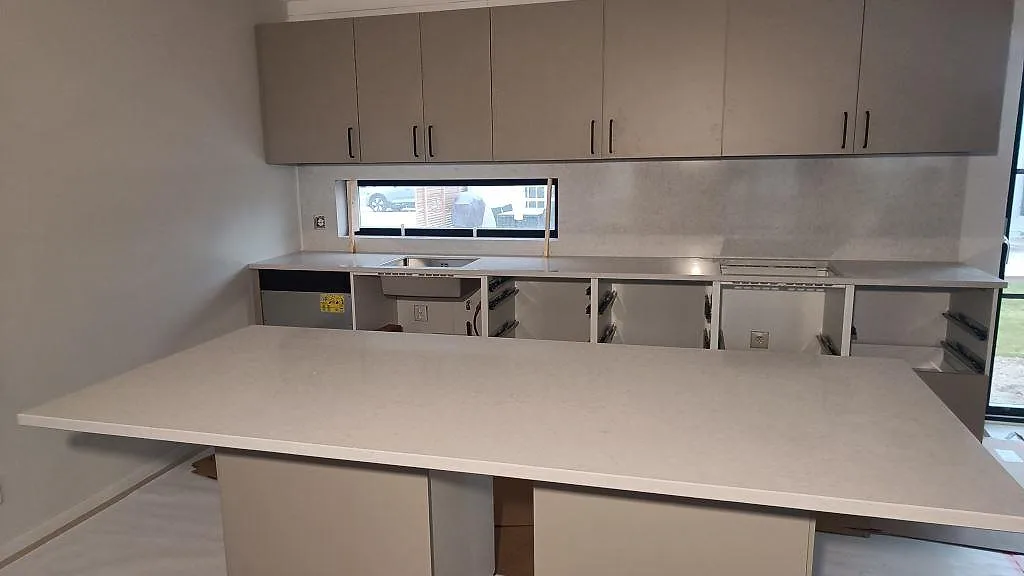 Køkkenbordplade og køkkenø i poleret Silestone Snowy Ibiza med matchande vægbeklædning i ett køkken i Skurup under montering.