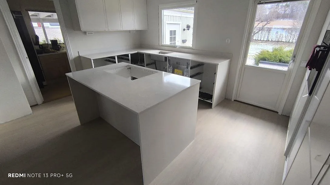 Køkkenbordplade i hvid Silestone Snowy Ibiza, poleret kvartskomposit, med køkkenø og bordplader längs väggarna i ett køkken i Söderköping.