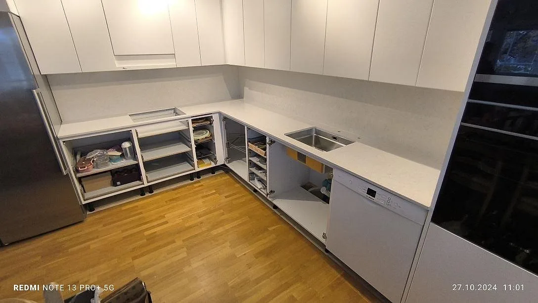 L-format køkken i Södertälje med poleret køkkenbordplade i lys Silestone Snowy Ibiza og hög stänkyta under montering.
