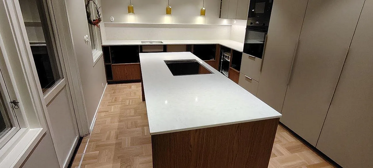 Poleret køkkenbordplade og køkkenø i hvid Silestone Snowy Ibiza, kvartskomposit, med kogeplade og väggbänkar i ett køkken i Spånga.