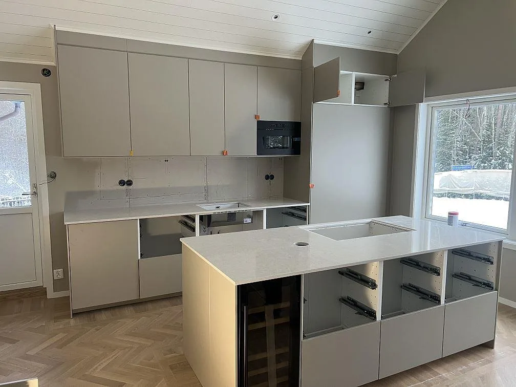 Køkkenbordplade og køkkenø i poleret Silestone Snowy Ibiza kvartskomposit, monterade i ett køkken under färdigställande i Stigtomta.