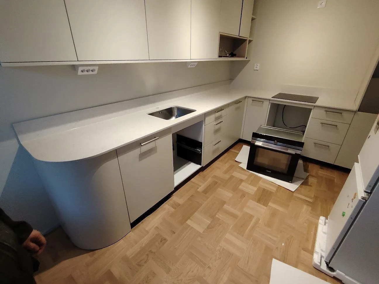 L-formad køkkenbordplade i poleret Silestone Snowy Ibiza, lys kvartskomposit med låg stänkkant og afrundet avslutning i ett køkken i Stockholm.