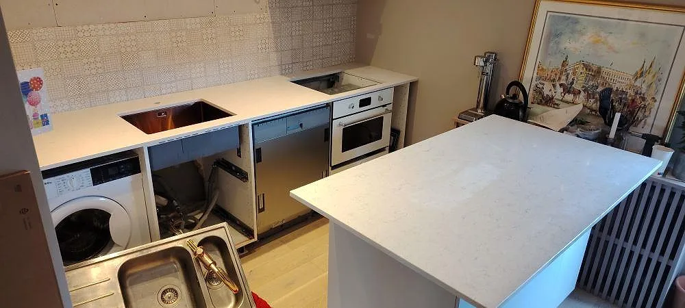 Køkkenbordplade i hvid Silestone Snowy Ibiza, 20 mm poleret komposit, med separat køkkenø og bänkrad längs væggen i ett køkken under montering i Stockholm.