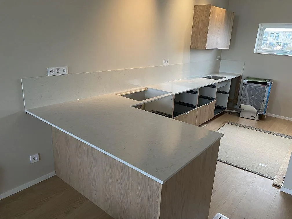 Køkkenbordplade i poleret Silestone Snowy Ibiza med halvö, stænkplade, hällöppning og diskhozon i ett køkken i Tygelsjö.