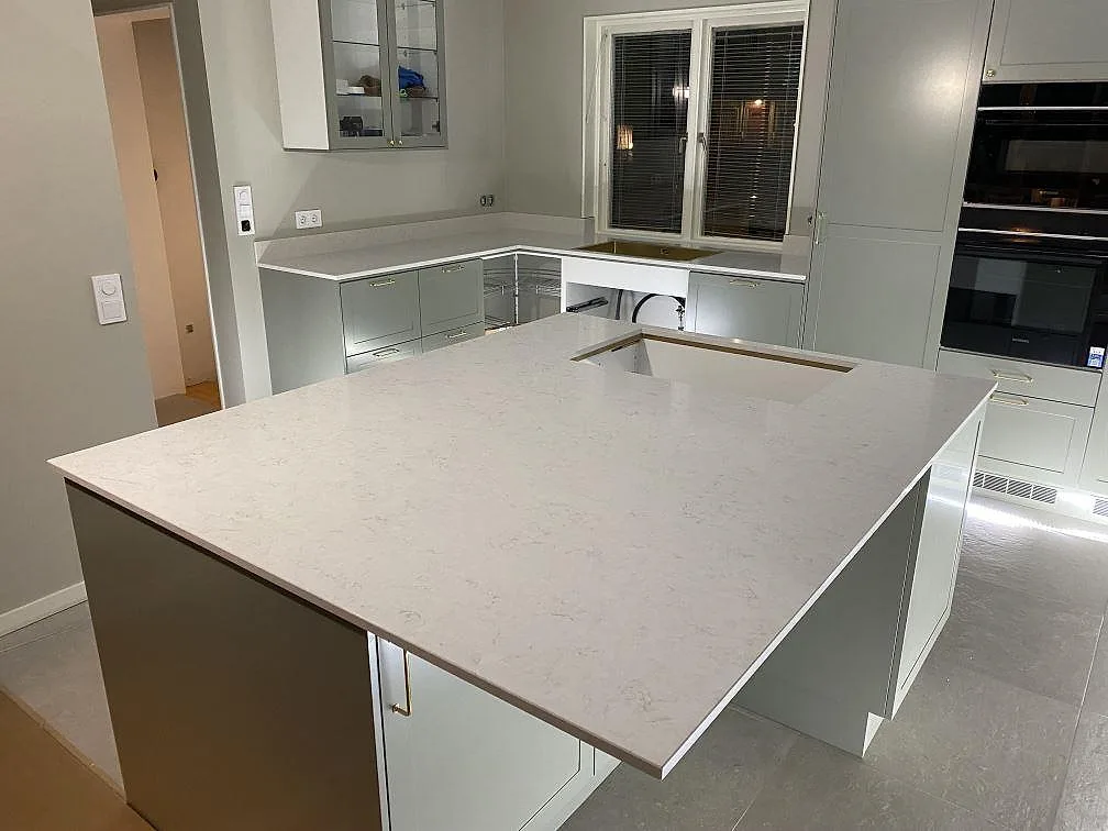 Køkkenbordplade og køkkenø i poleret Silestone Snowy Ibiza, lys kvartskomposit, med hälluttag og stænkplade i ett køkken i Växjö.
