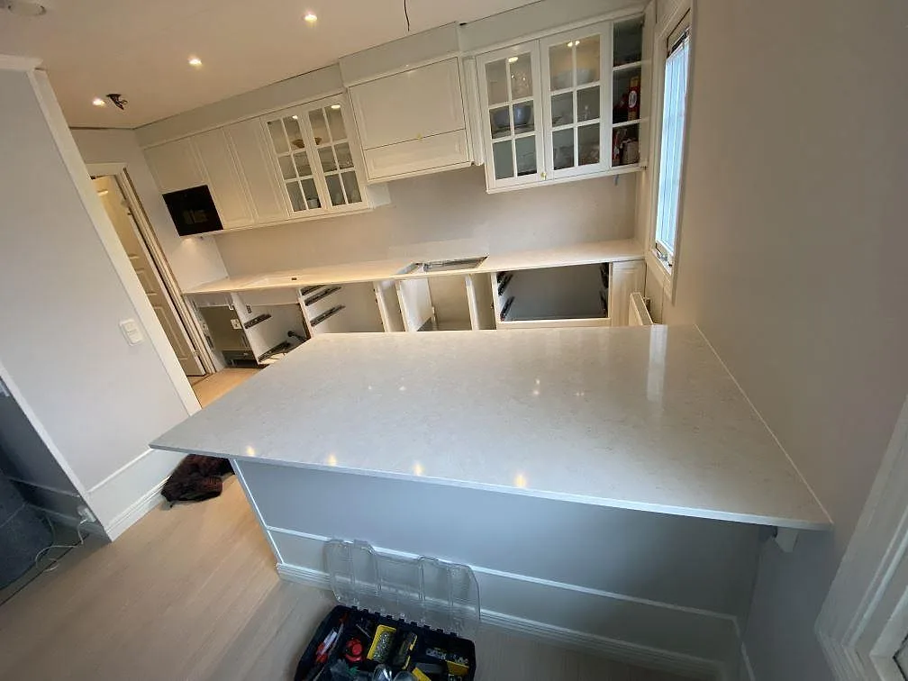 Køkkenbordplade og køkkenø i poleret Silestone Snowy Ibiza, lys kvartskomposit, monterade i ett køkken i Vallberga under pågående inredning.