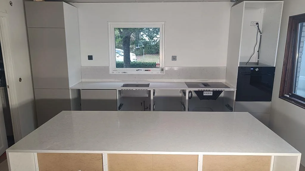 Køkkenbordplade og køkkenø i poleret Silestone Snowy Ibiza, lys kvartskomposit, med stenklädda sidor og bakre bänkrad i ett køkken i Viken.