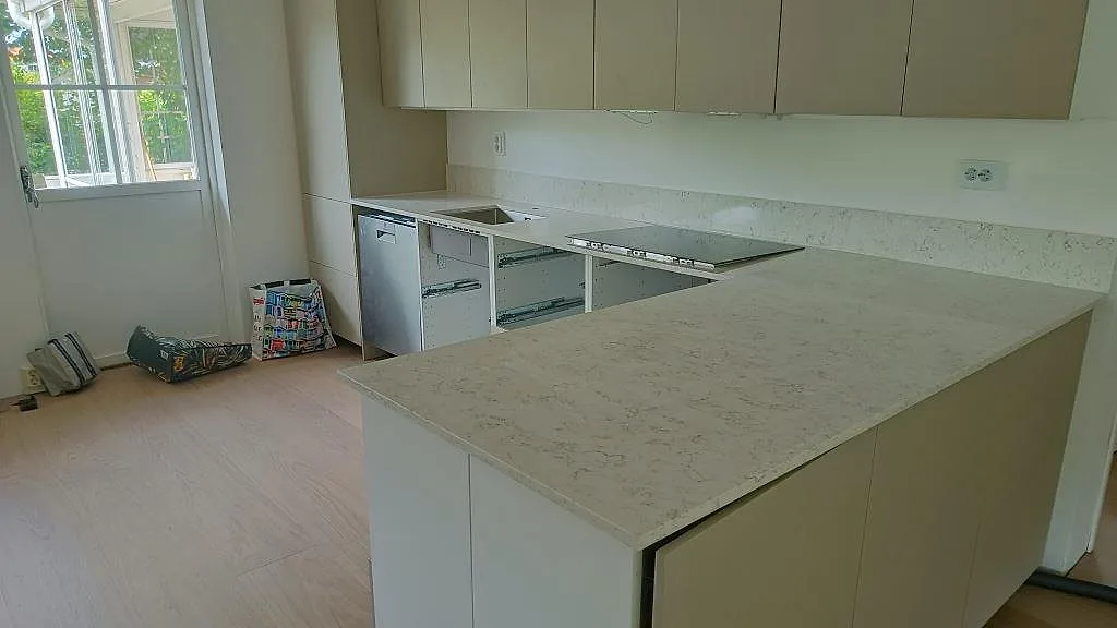Køkkenbordplade i hvid Silestone White Arabesque med blød grå åretegning, poleret, vinklad bordplade med uppvikt stänkkant, induktionshäll og diskhoplats i ett køkken under montering i Göteborg.