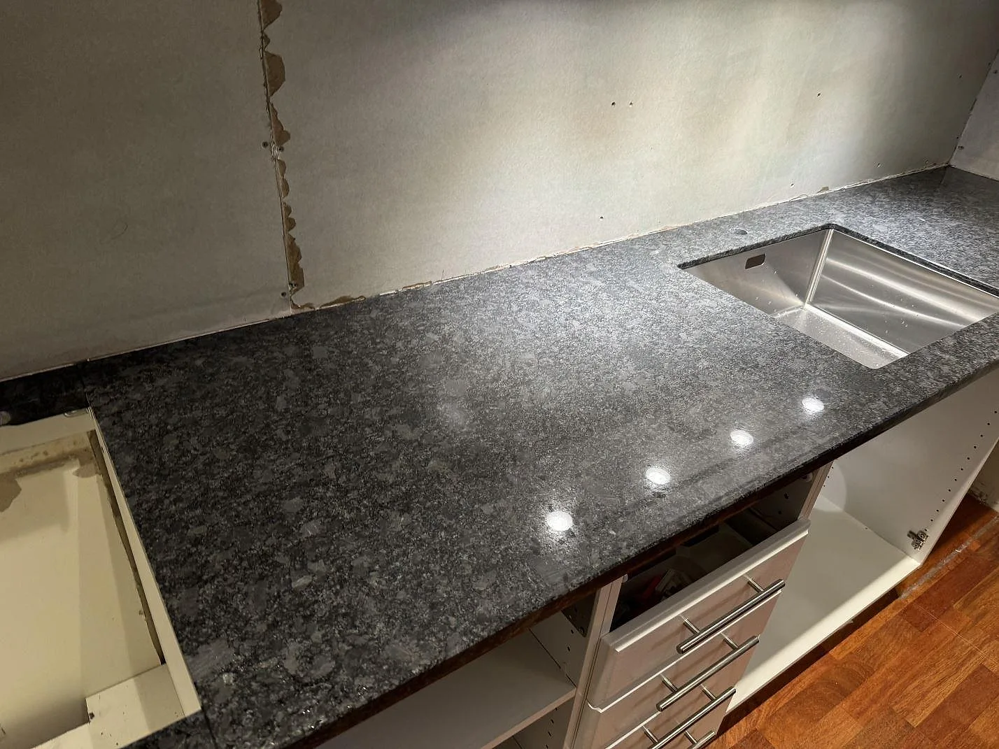 Poleret køkkenbordplade i Steel Grey granit med rostfri vask og mørk stenstruktur i ett køkken i Lund.