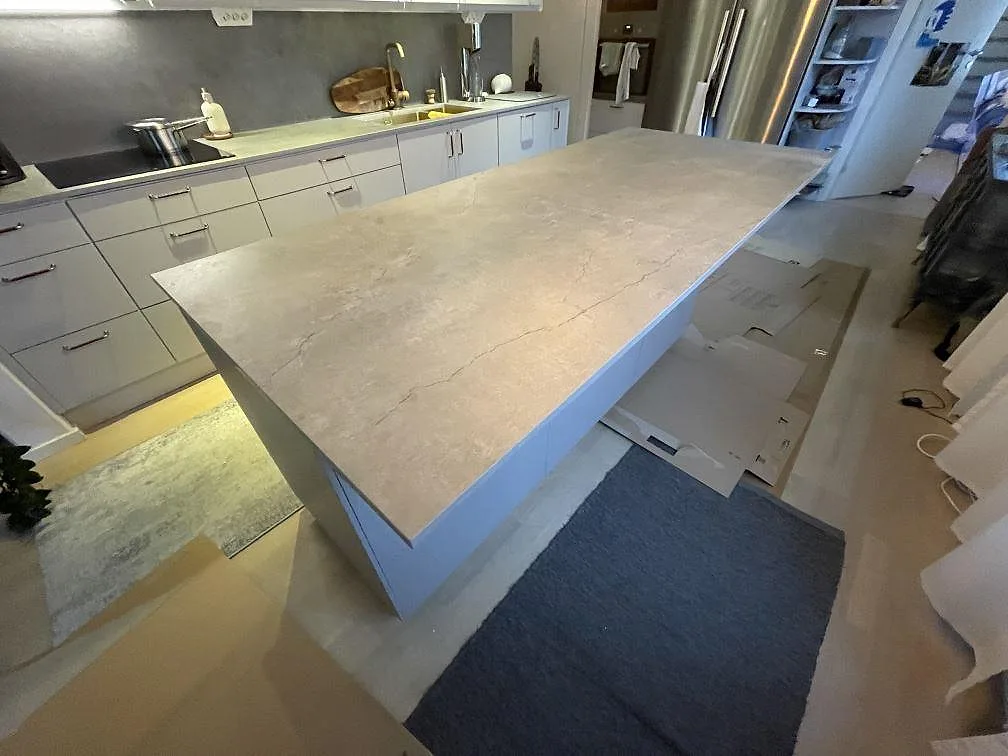 Stor køkkenø i beige Dekton Soke keramik, mat overflade, som frihängande mittpunkt i ett køkken i Stockholm med vask og kogeplade på den bakre bänkraden.