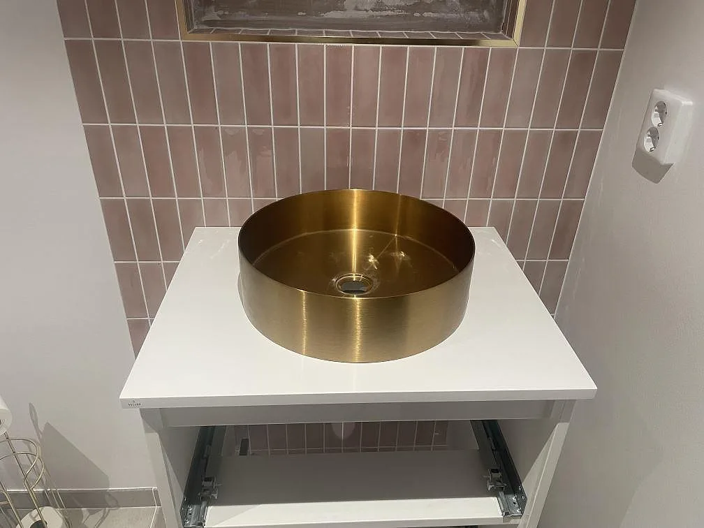 Badrumsbänkskiva i hvid Technistone Crystal Absolute White, poleret komposit, med rund guldfärgad tvättställsskål og rosa kakel i Enköping.