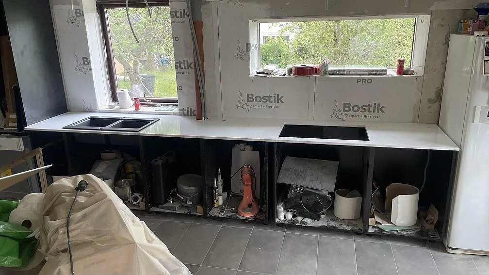Køkkenbordplade i poleret Technistone Crystal Absolute White, hvid kvartskomposit, monteret längs fönsterväggen i ett køkken i Härryda.