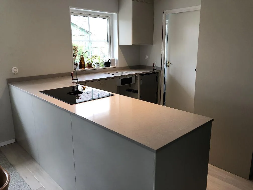 Køkkenbordplade i poleret Technistone Crystal Absolute White, lys komposit, med sort kogeplade og halvö i ett køkken i Skanör.