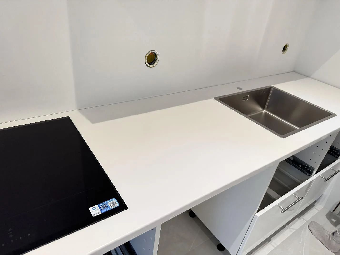 Køkkenbordplade i hvid Technistone Crystal Absolute White komposit, poleret, med kogeplade og rostfri vask i ett køkken under montering i Trelleborg.
