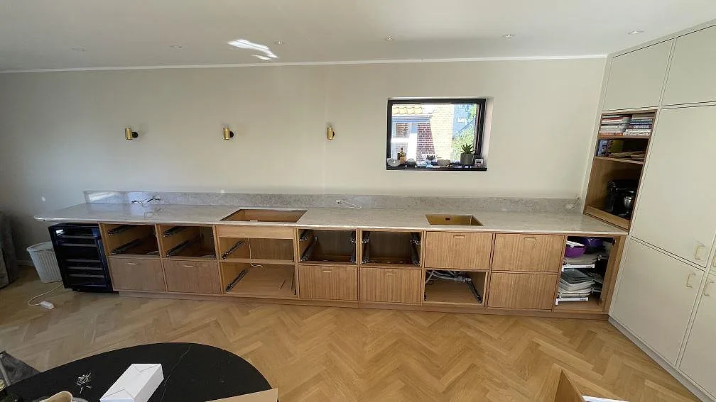 Lang køkkenbordplade i poleret Technistone Glencoe med uppvikt stänkkant og synliga udskæring i ett køkken i København S.