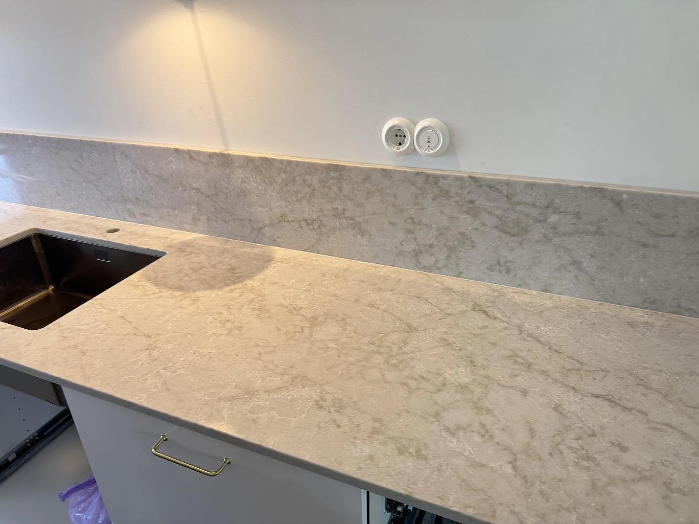 Køkkenbordplade i poleret Technistone Glencoe kvartskomposit med låg stänkkant og rostfri vask under montering i Malmö.