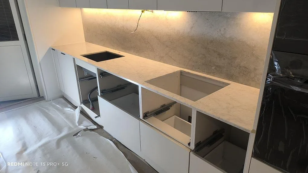 Køkkenbordplade i lys poleret Technistone Glencoe komposit med öppningar for vask og kogeplade i ett køkken under montering i Norrköping.