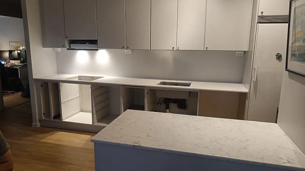 Køkkenbordplade og køkkenø i hvid Technistone Mystery White, poleret kvartskomposit, med rostfri vask og hällurtag i ett køkken i Bjärred.