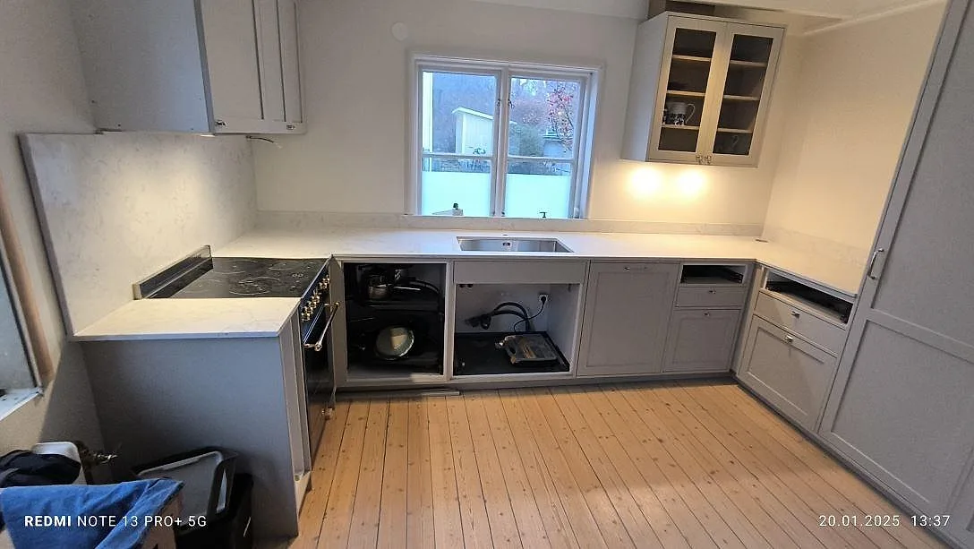 Køkkenbordplade i 20 mm poleret Technistone Mystery White, lys kvartskomposit längs vægge og vindue i ett køkken under montering i Bromma.