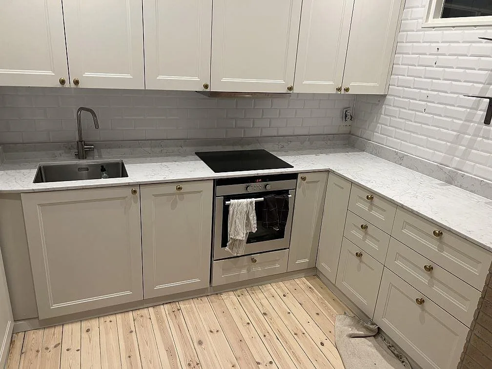 Køkkenbordplade i hvid Technistone Mystery White, poleret komposit, med synlig vask og kogeplade i ett L-format køkken i Stockholm.