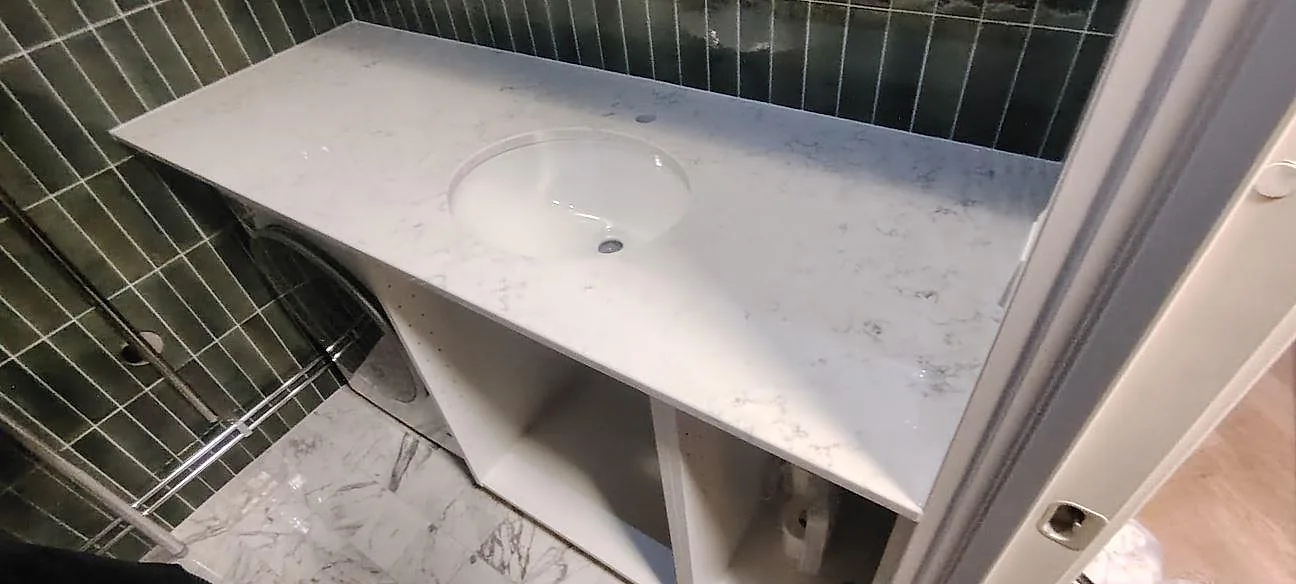 Badrumsbänkskiva i poleret Technistone Mystery White kvartskomposit med rund tvättställsöppning og kaklade vægge i Stockholm.