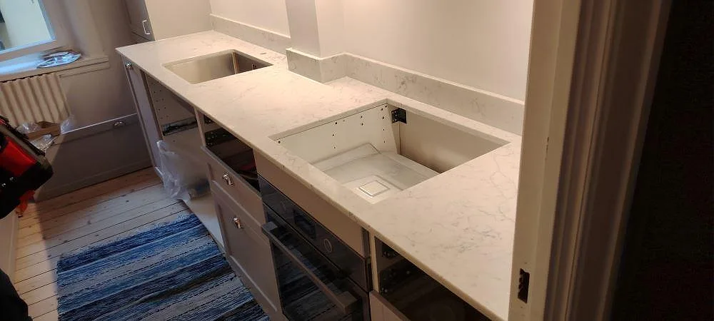 Køkkenbordplade i hvid Technistone Mystery White, poleret kvartskomposit, med låg stänkkant og synliga udskæring i ett køkken i Stockholm.
