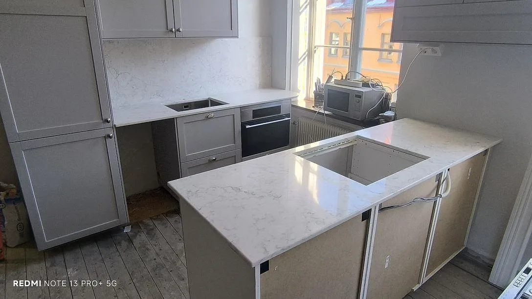 Køkkenbordplade og køkkenø i lys Technistone Mystery White, poleret kvartskomposit, under montering i ett køkken i Stockholm.