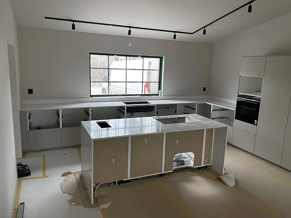Køkkenbordplade i Technistone Noble Arco, 20 mm poleret lys kvartskomposit, monteret på køkkenø og bänkrader i ett køkken under montering i Köping.