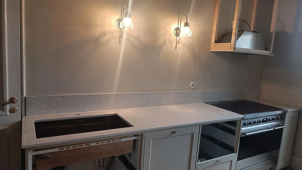 Køkkenbordplade i Technistone Noble Arco, poleret lys kvartskomposit med grå åretegning, låg stänkkant og fristående komfur i Malmö.